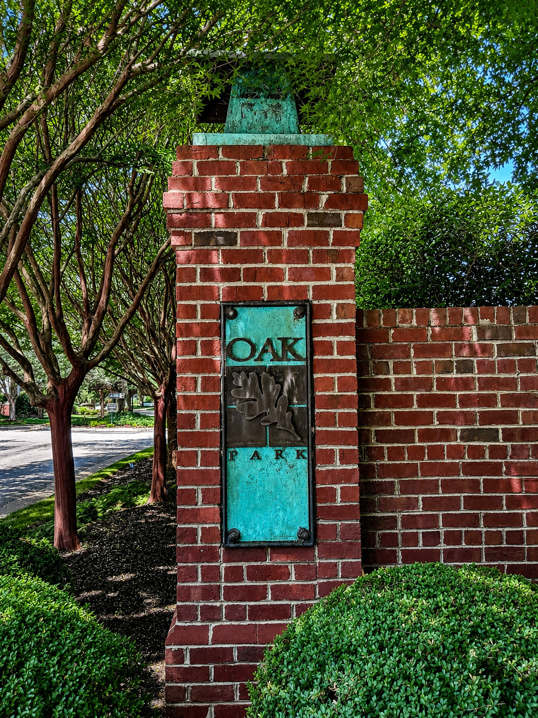 The brick and patinated copper Oak Park entrance pillar, framed by crepe myrtles and boxwoods